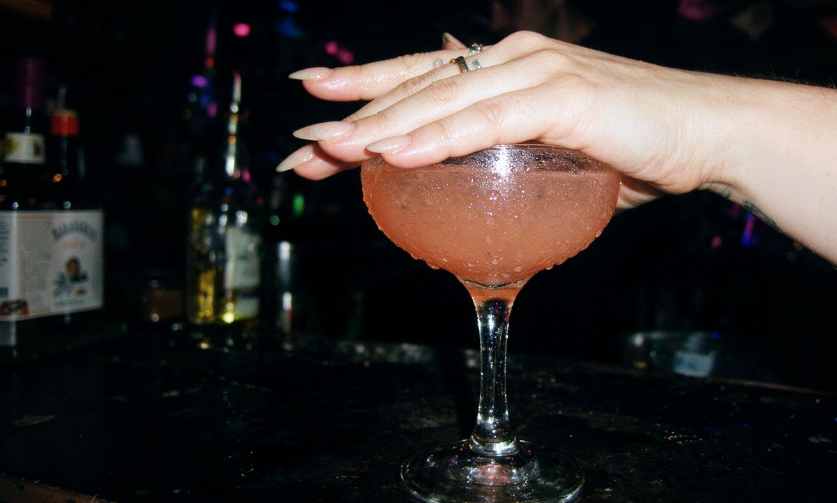 Mano de una mujer tapando una copa de cóctel sobre la barra de un bar